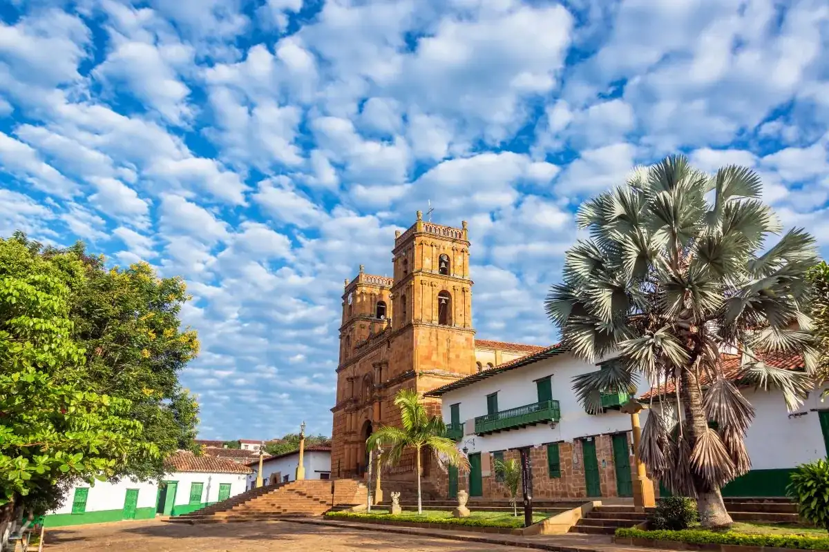 Fachada de la catedral de Barichara en piedra amarilla, entre palmas y un cielo de nubes