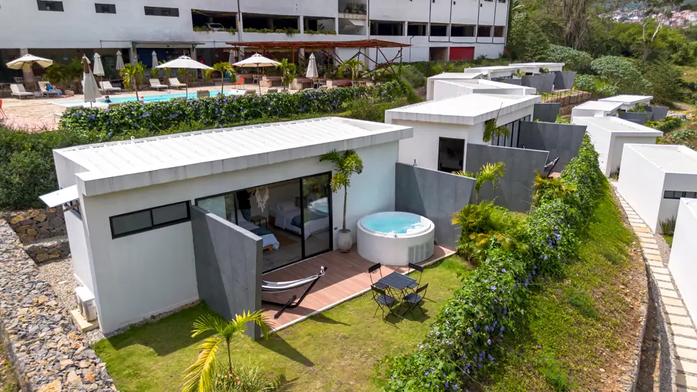 Cabaña blanca con jacuzzi, hamaca y jardín propio, con la piscina del hotel detrás
