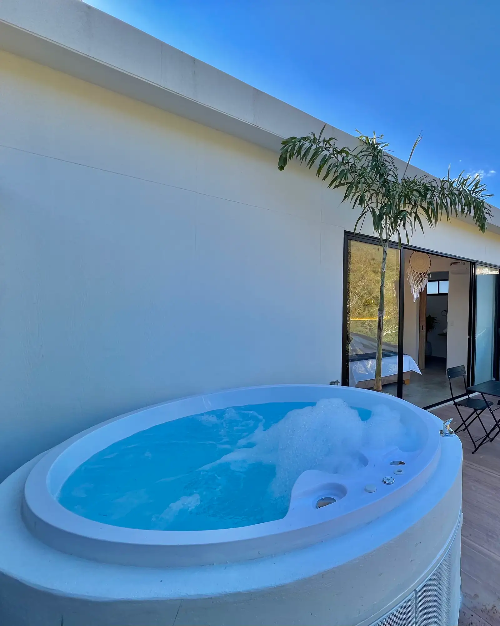 Jacuzzi redondo con burbujas en la terraza de madera del Glamping Deluxe, bajo el cielo azul