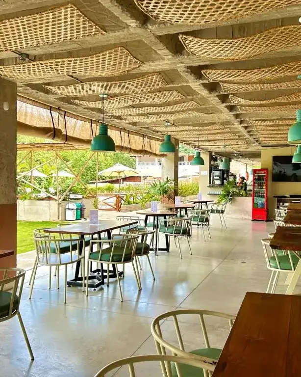 Comedor de Alaia con sillas verdes de metal, lámparas colgantes y el techo de esterilla tejida